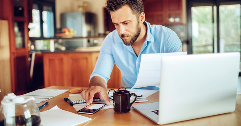 Man using phone calculator at dining room table.