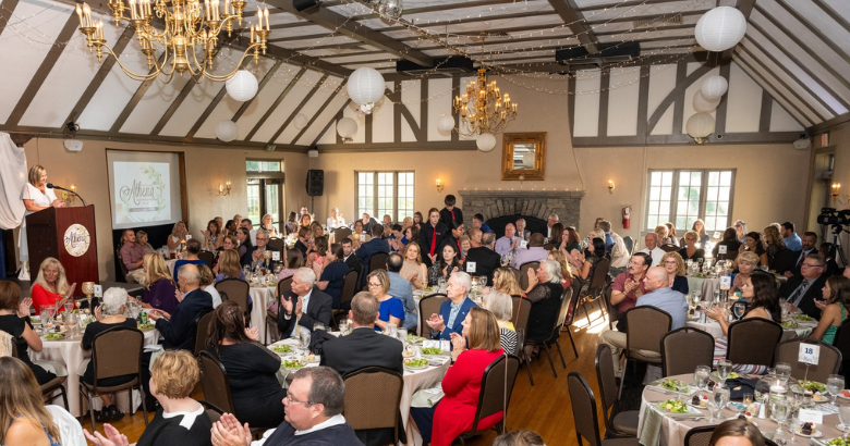 a room full of community members applaud as a speaker presents an award