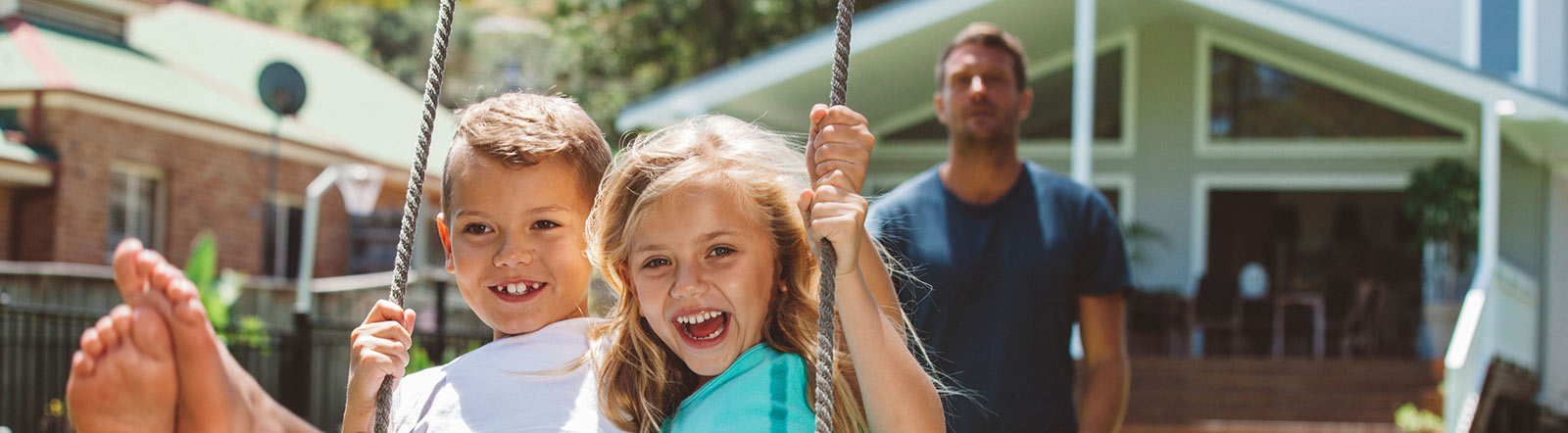 Dad pushing kids on swing in backyard.