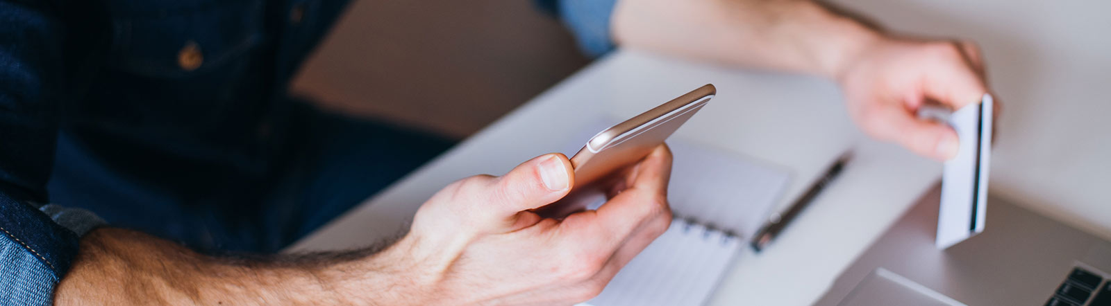 Man holding card and phone on laptop.