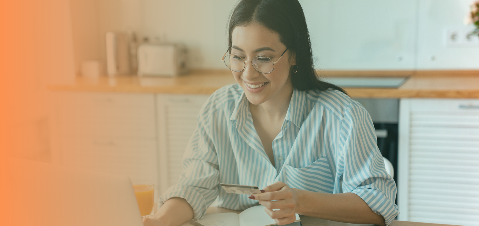 female with brown hair and glasses holds a credit card while using laptop