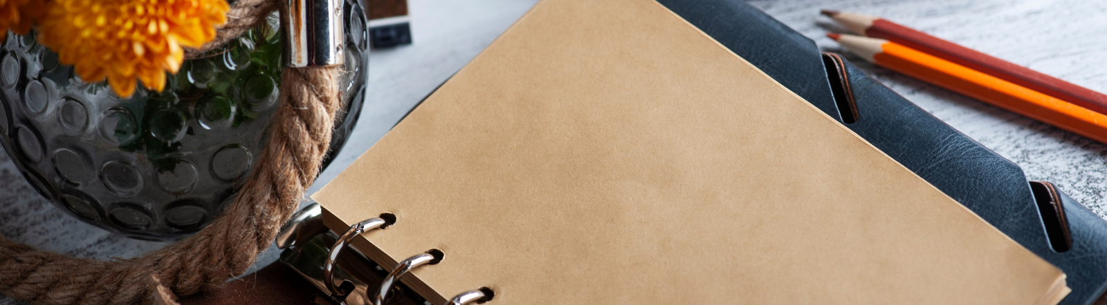 notebook surrounded by flower vase and pencils