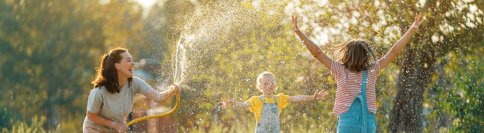 mom and two girls playing with hose in back yard